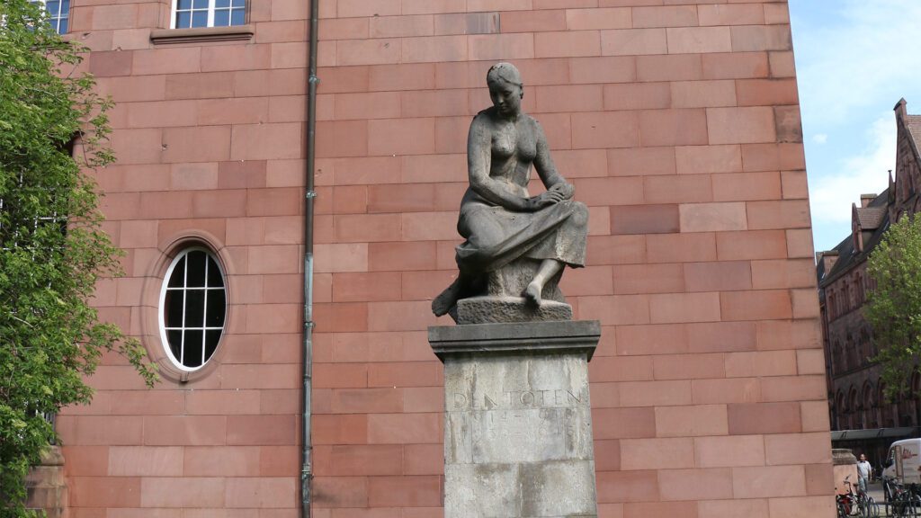 Die Statue auf dem Rasen des KGI steht für die trauernde Alma Mater, welche der Bildhauer Arnold Rickert im Nachgang des ersten Weltkrieges fertigte. Heute erinnert sie als Denkmal an die in den Weltkriegen gefallenen Mitglieder der Universität.