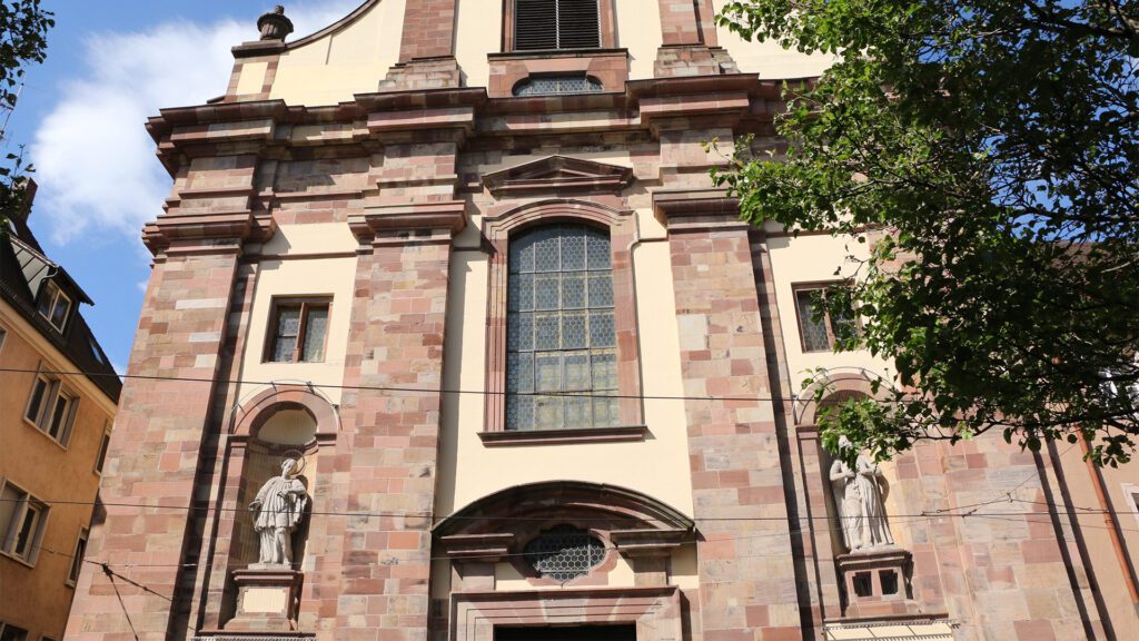 Statuen an der Universitätskirche: Links ist Aloysius von Gonzaga und rechts Stanislaus Kostka zu sehen. „Beide haben im 16. Jahrhundert gelebt, beide waren Jesuiten und beide sind jung gestorben“, sagt Wilhelm Gros. Aufgrund ihrer Jugend sollten sie als Patrone für junge Menschen dienen: Aloysius vor allem in Berufsfindungsfragen und Stanislaus hauptsächlich in Fragen der inneren Glaubenskämpfe. Wer sie gefertigt habe, sei unklar.